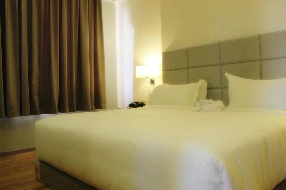 A hotel room with a large bed, a nightstand, a lamp, and a window with curtains.