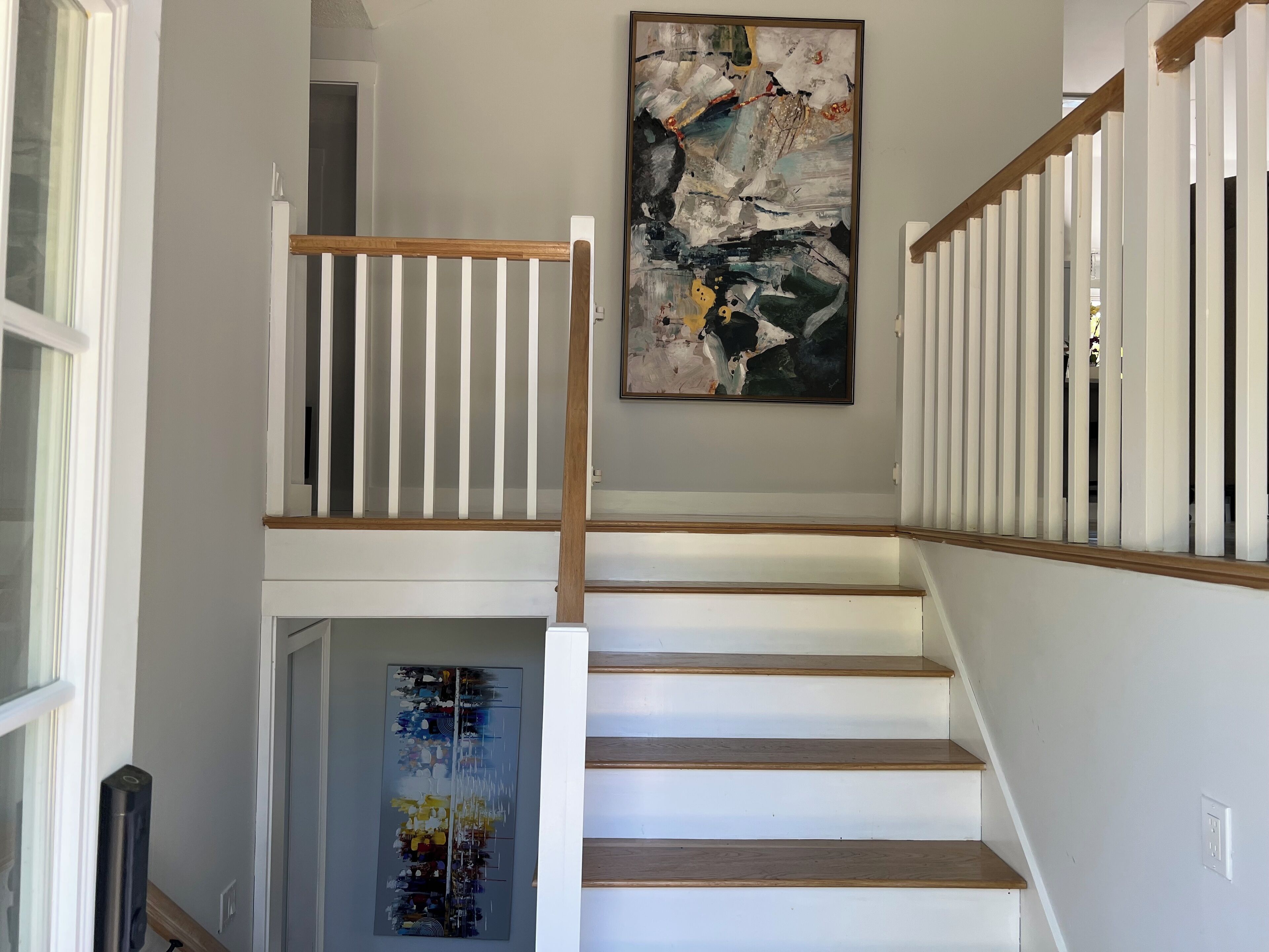 A staircase with white railings and wooden steps, leading to a landing with a large abstract painting.