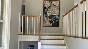 Una escalera con barandillas blancas y peldaños de madera, que conduce a una plataforma con un cuadro abstracto de gran tamaño.