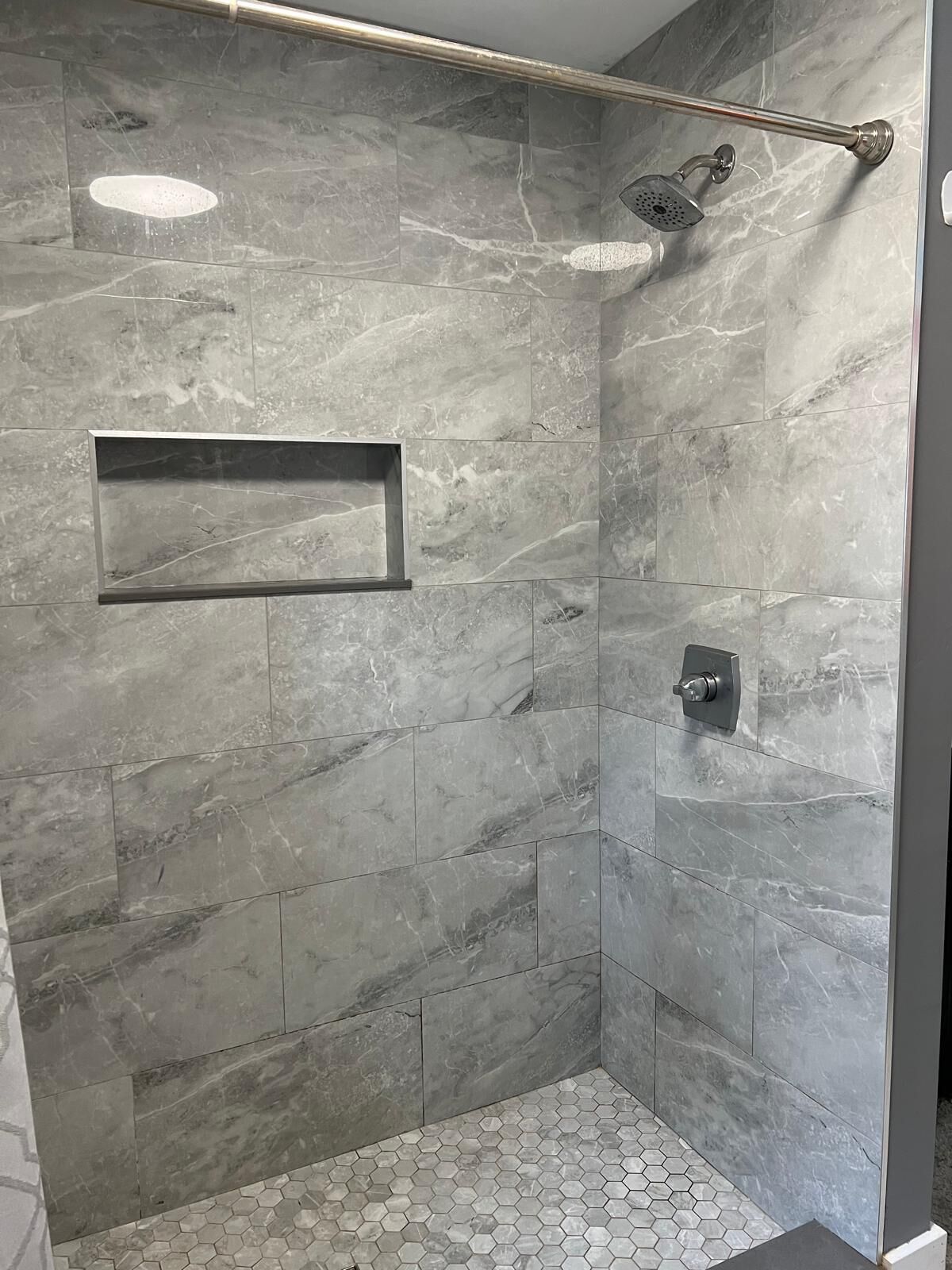 Une douche à l’italienne avec une paroi en verre, une étagère intégrée et une pomme de douche à pluie.