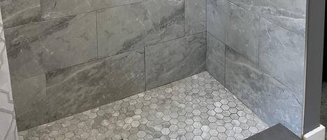 Une douche à l’italienne avec une paroi en verre, une étagère intégrée et une pomme de douche à pluie.
