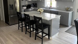 Una cocina moderna con armarios grises, un refrigerador de acero inoxidable, una isla central con sillas e iluminación colgante.
