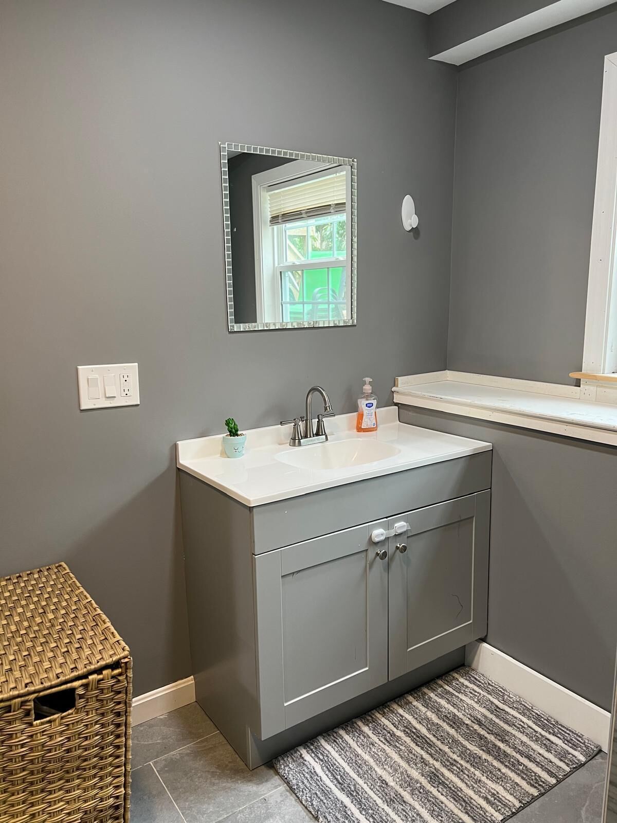 A bathroom with a grey wall, a white sink, a small potted plant, and a striped rug.