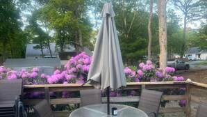 Un patio al aire libre con una mesa redonda de vidrio, dos sillas y un paraguas gris.
