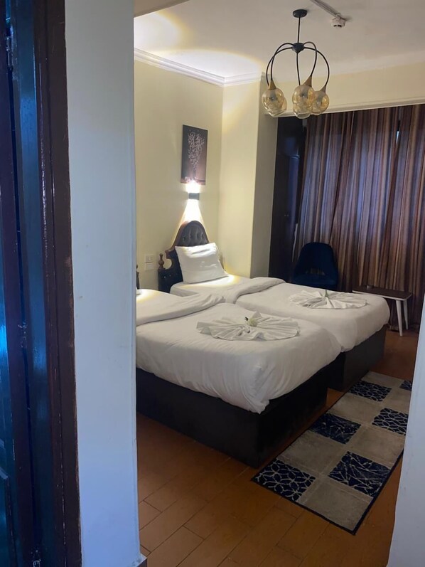 Una habitación de hotel con cama, escritorio, silla, lámpara y ventana con cortinas.
