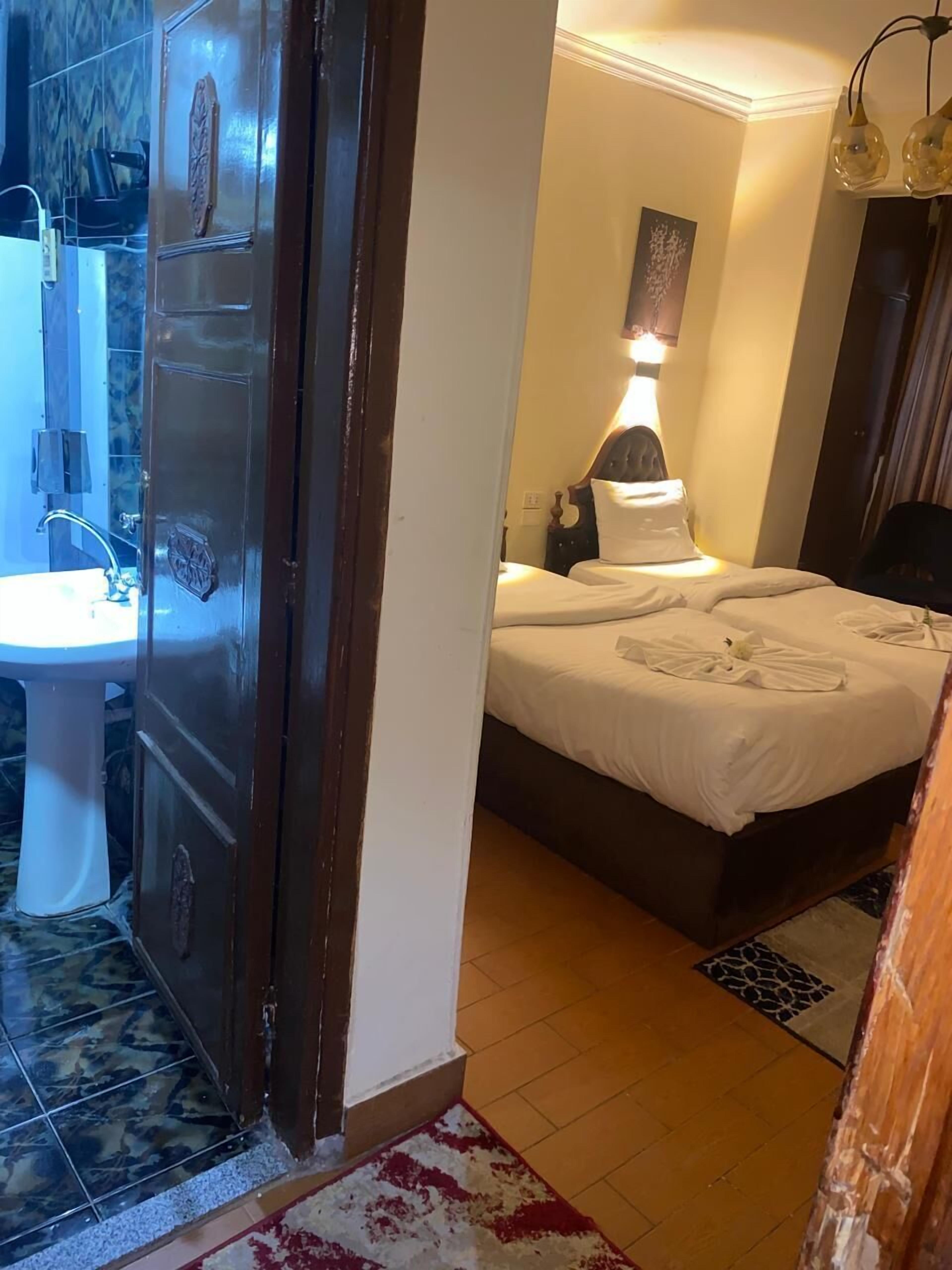 A hotel room with a bed, bedside table, lamp, and a bathroom with a sink and mirror.