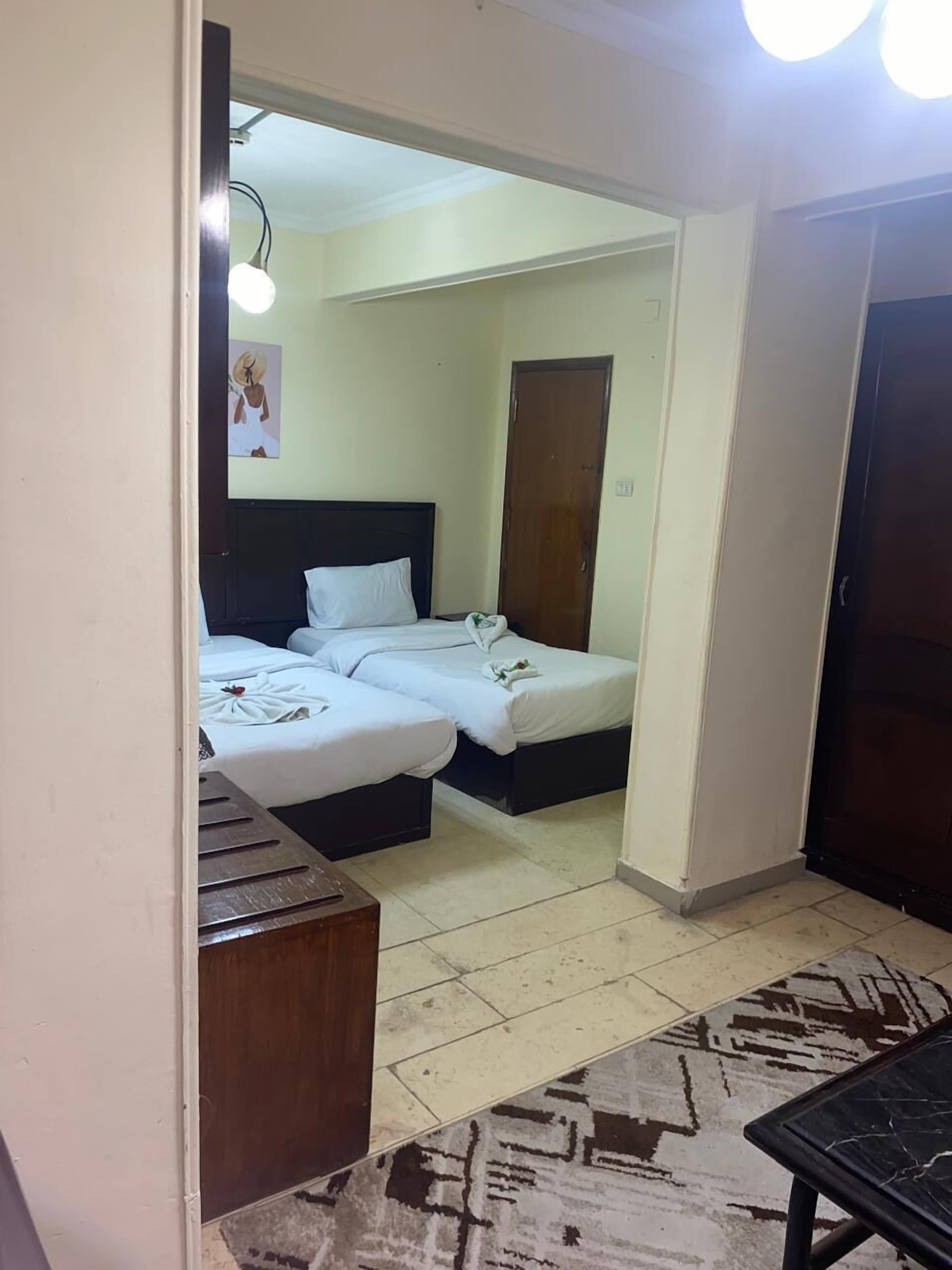 A small, clean room with two single beds, a wooden bench, a patterned rug, and a door leading to another room.