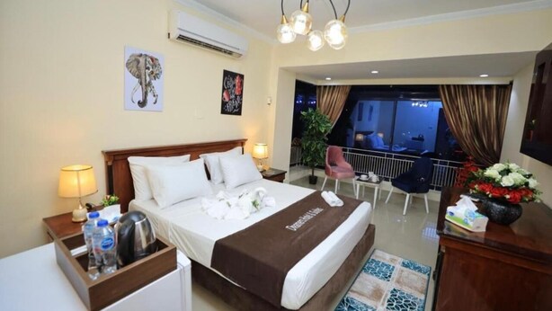A hotel room with a large bed, a desk, a chair, a balcony with a view, and a chandelier. - Dreamers Cairo Hotel (Giza)
