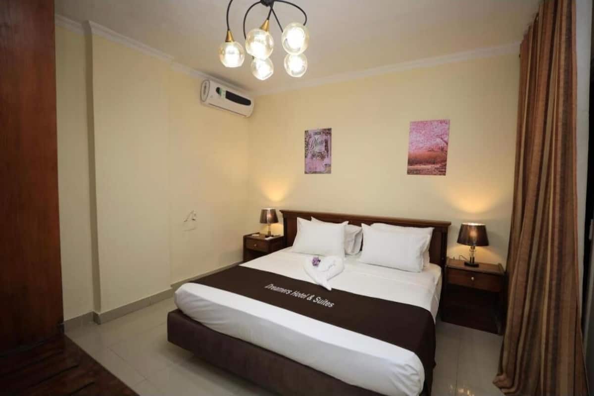 A hotel room with a large bed, two bedside tables with lamps, a ceiling light fixture, and two wall-mounted pictures.