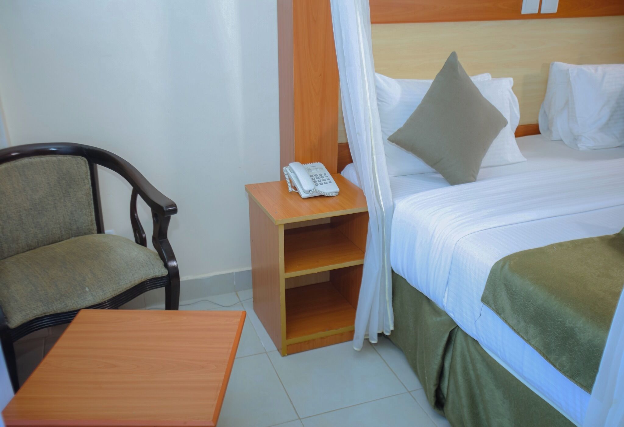 Habitación de hotel con cama, mesita de noche con teléfono, una silla y una pequeña mesa de madera.