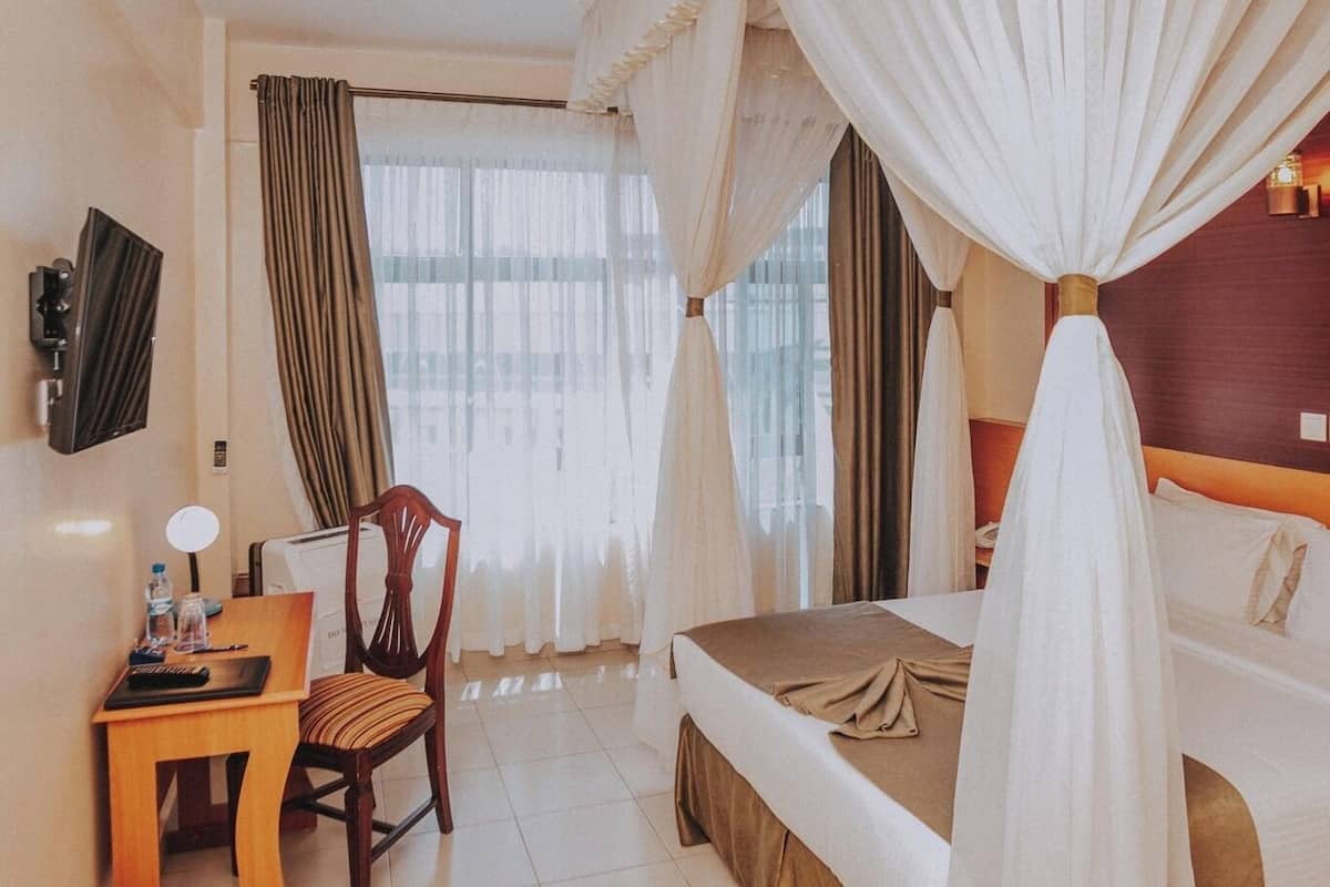 A hotel room with a bed, a desk, a chair, and curtains.
