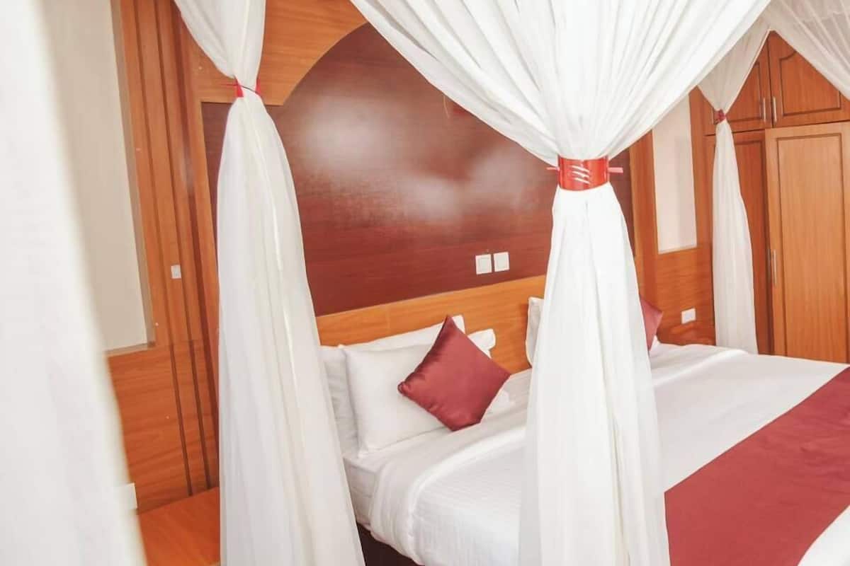 A hotel room with a bed, wooden headboard, and a red accent pillow.