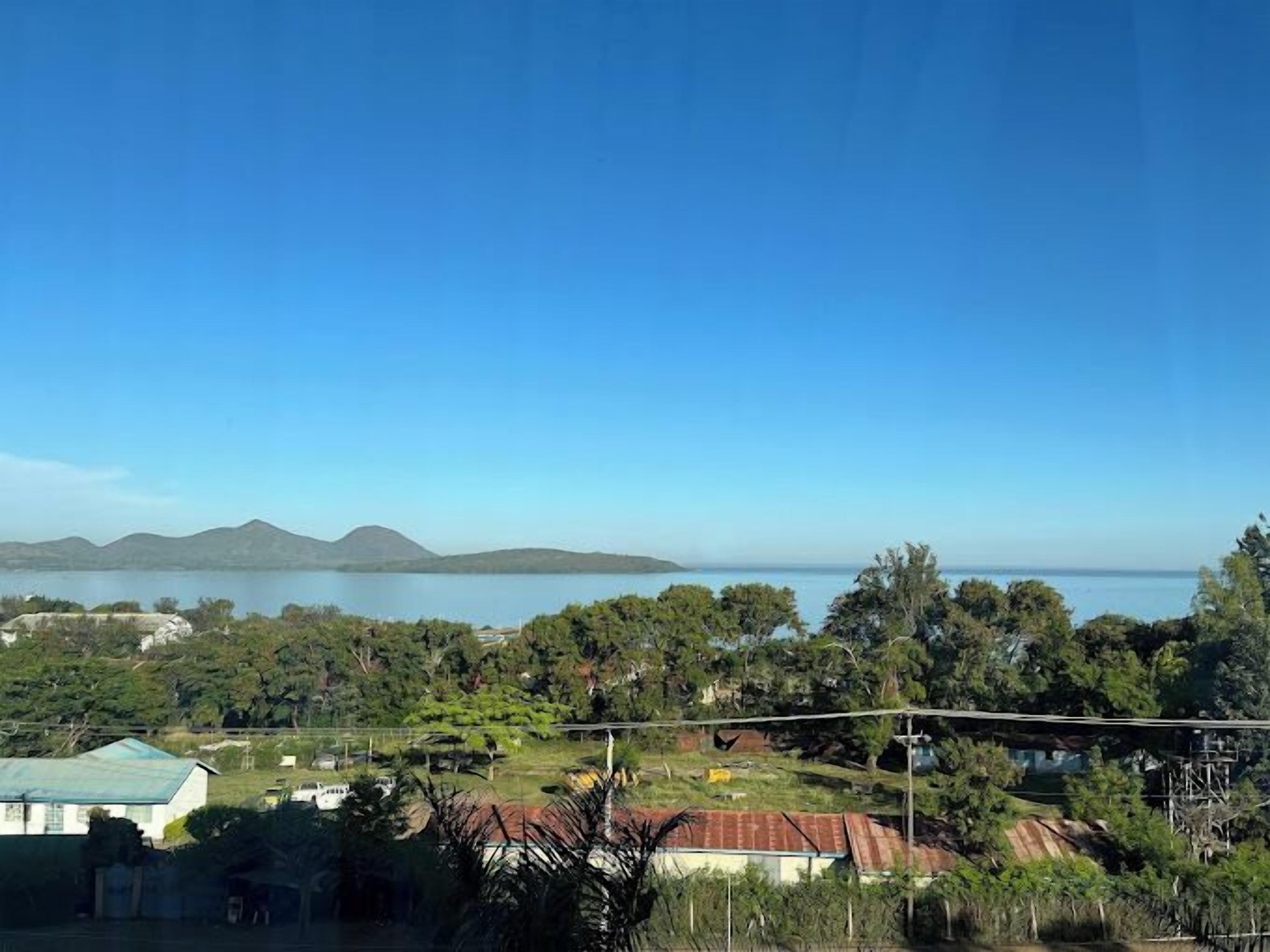 Paisatge costaner amb vista al mar, turons a la distància i una combinació d'edificis residencials i vegetació.