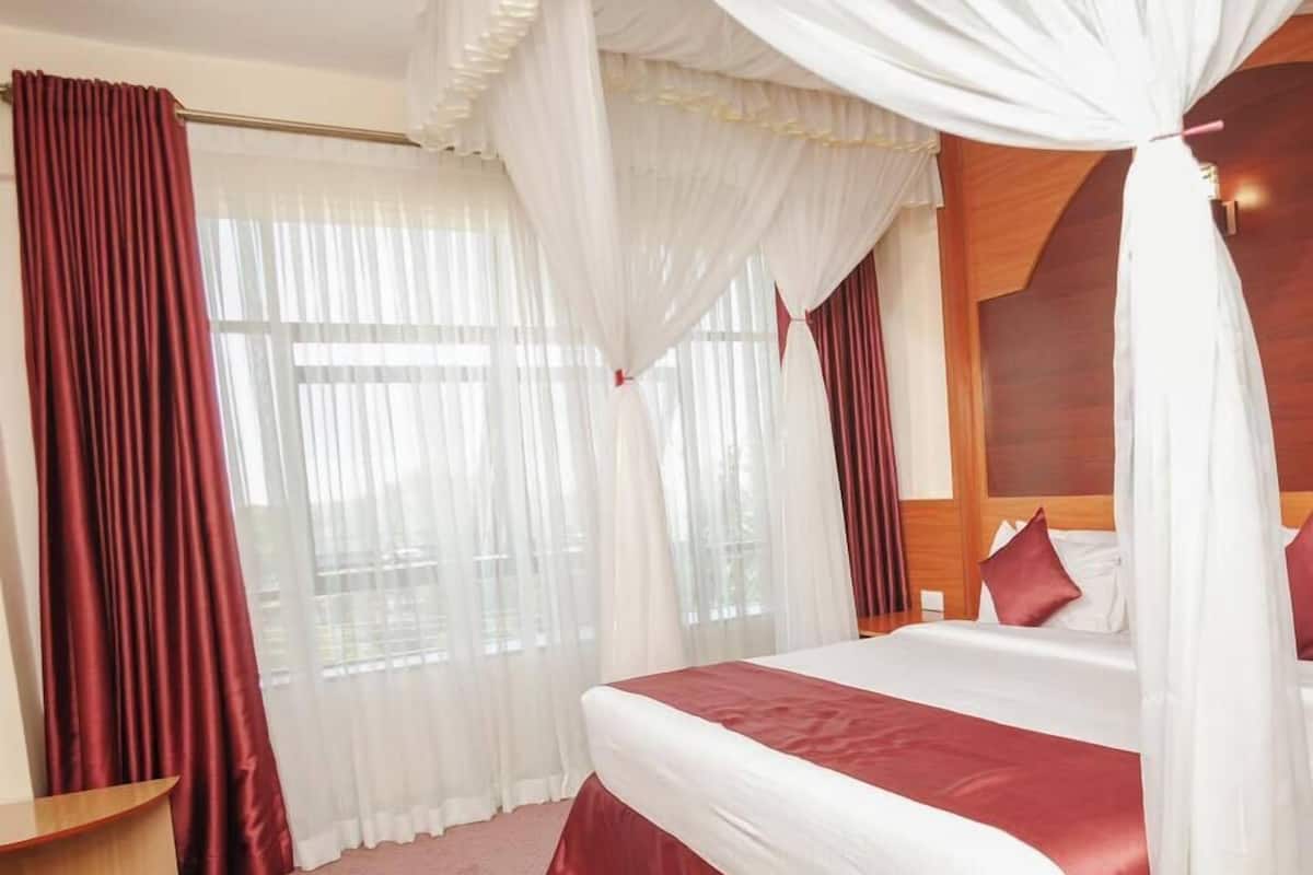 A hotel room with a large bed, red and white bedding, a wooden headboard, and a canopy bed.