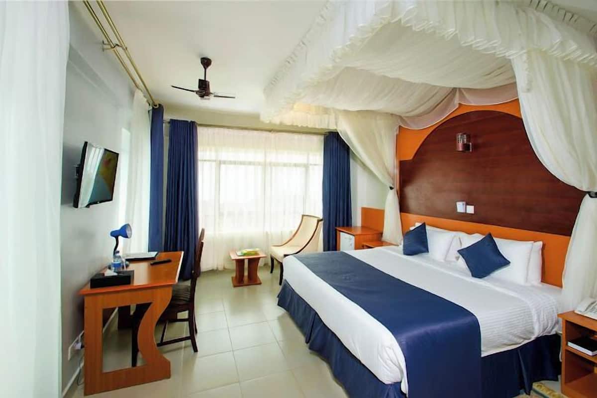 A hotel room with a large bed, a desk, a chair, a television, and a ceiling fan.