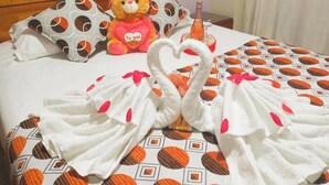 A bed with a patterned bedspread, a teddy bear, and two towels arranged in swan shapes. - HOTEL DESTINO AVENTURA PERU (Chanchamayo)