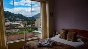 A hotel room with a large window offering a view of a hillside town. - HOTEL DESTINO AVENTURA PERU (Chanchamayo)