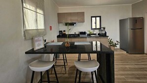Una cucina moderna con un piano di lavoro nero, due sgabelli da bar bianchi, un frigorifero in acciaio inossidabile e una finestra con persiane.
