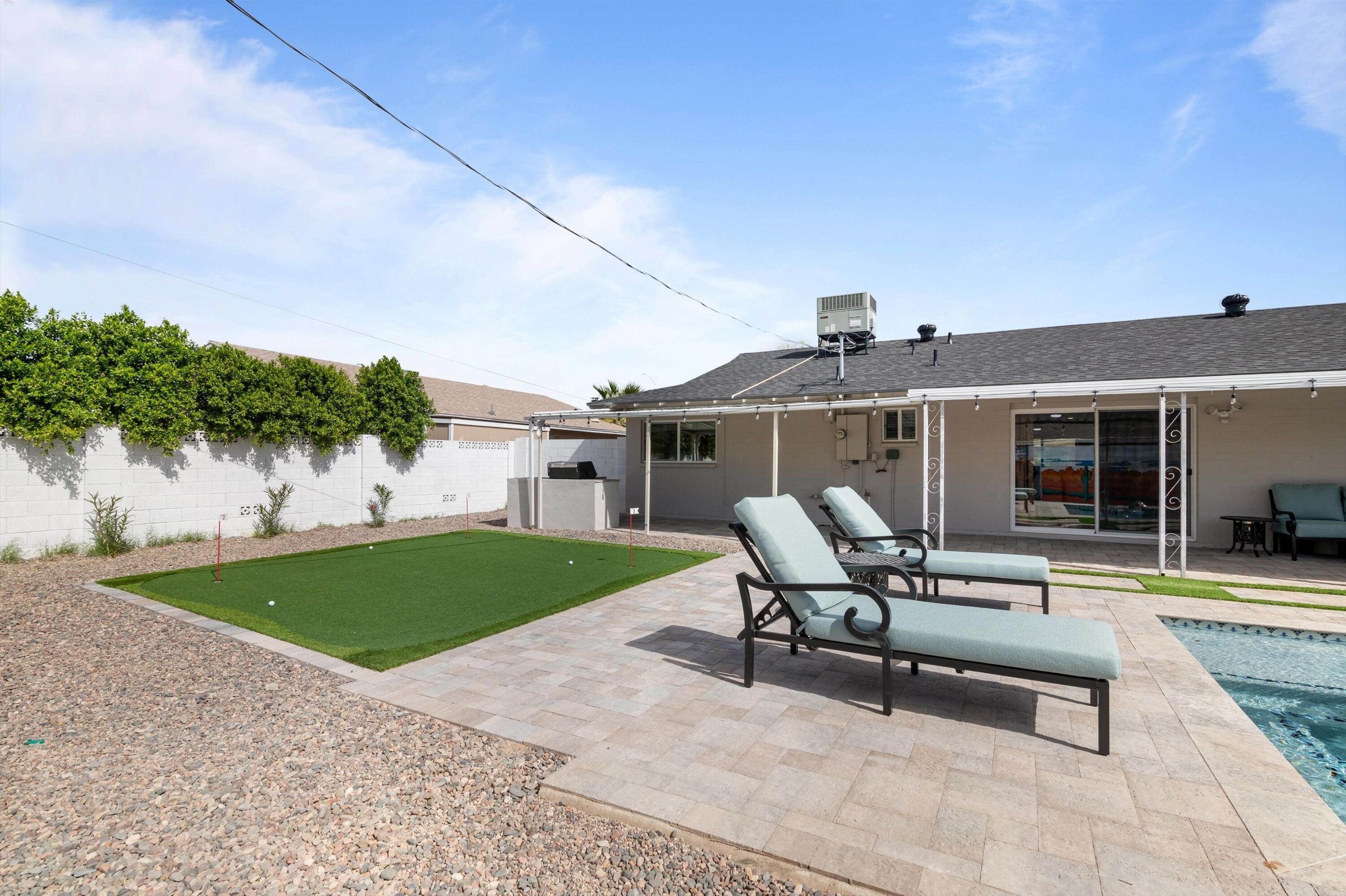 Un patio trasero con piscina, dos sillones de jardín, una mesa de patio y un pequeño césped.