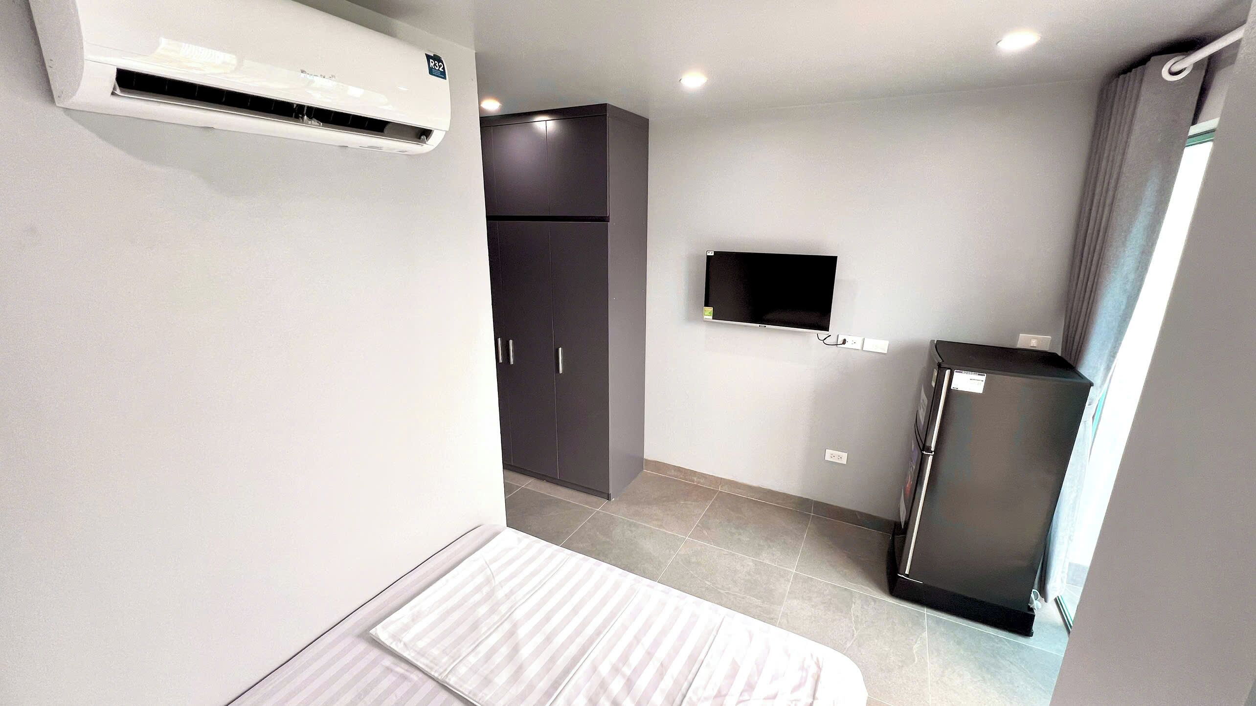 Habitación de hotel compacta con cama, armario, televisor y refrigerador.