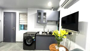 A compact kitchen with a washing machine, a sink, and a small dining area with a vase of yellow flowers. - Era Apartment Cat Linh (Hanoi)