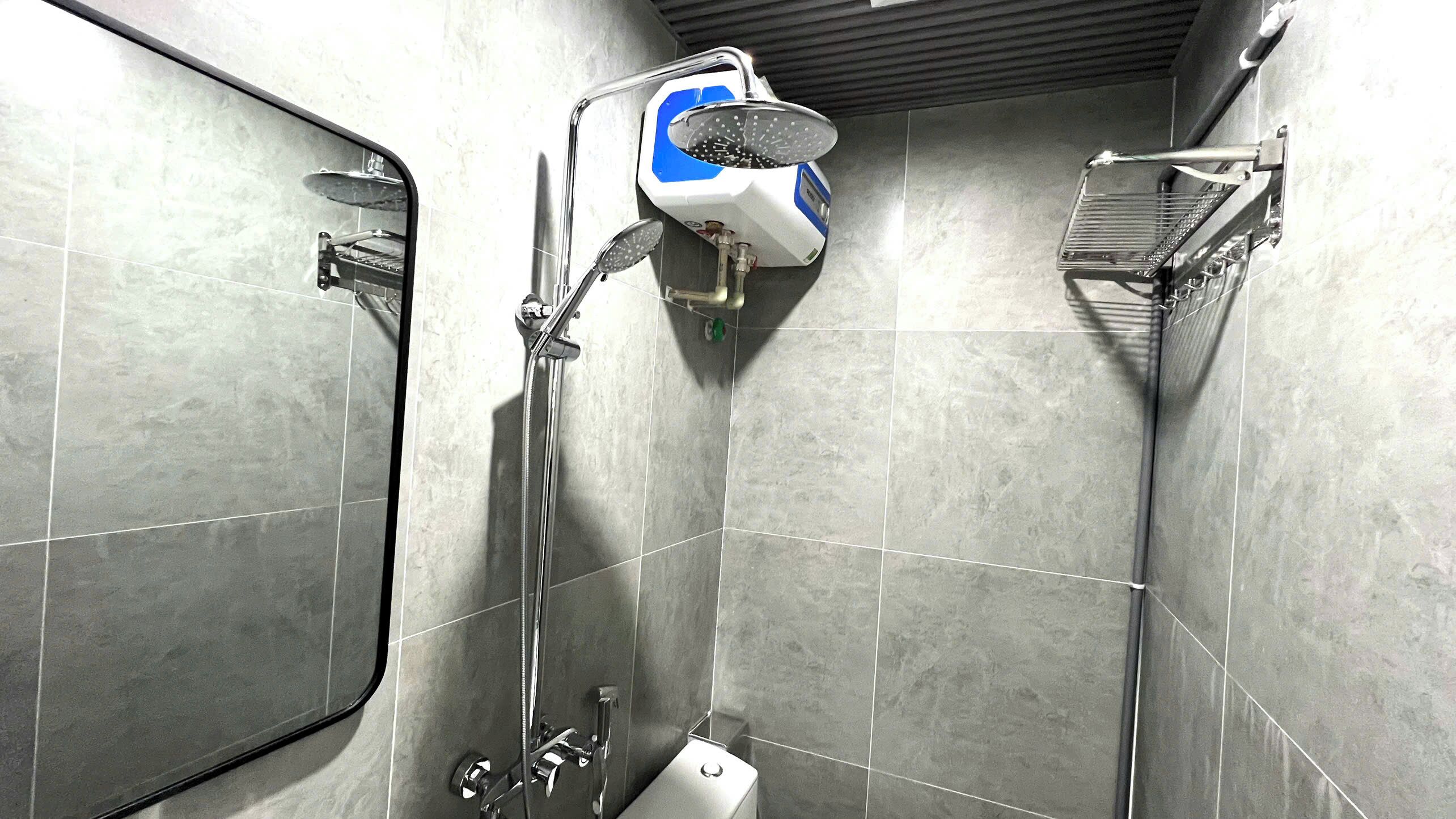 Casa de banho com azulejos cinzentos, chuveiro manual, lavatório fixado na parede e sanita.