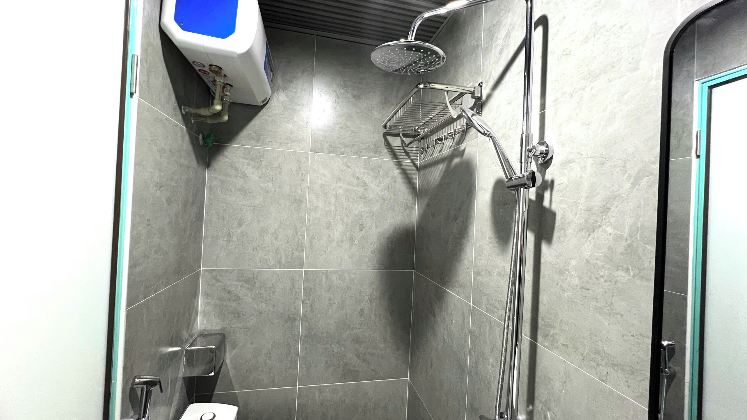 Eine kleine, geflieste Duschkabine mit Handbrause und am Wand montiertem Wasserhahn.