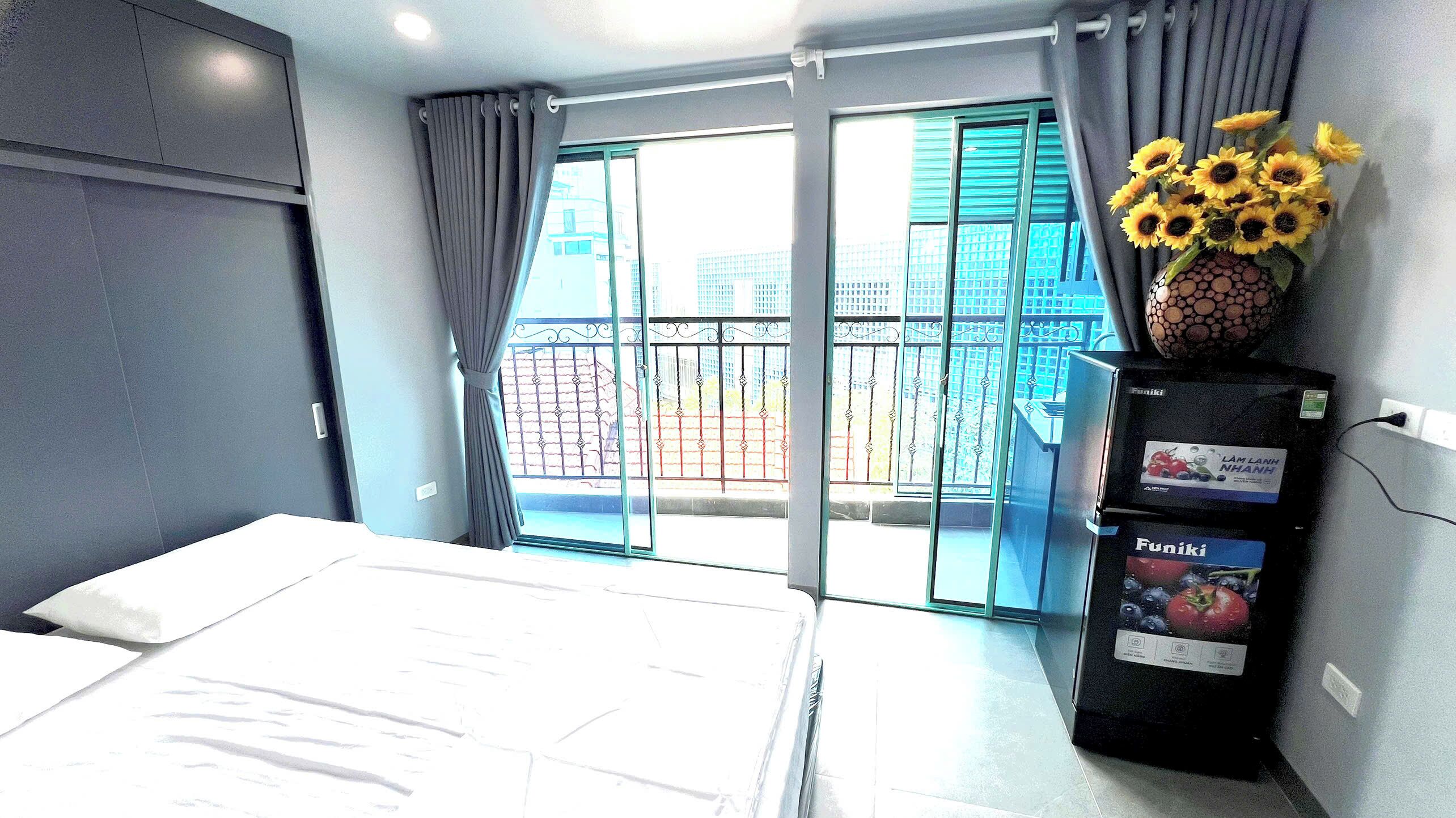 A hotel room with a bed, a minibar, a window with curtains, and a view of the outside.