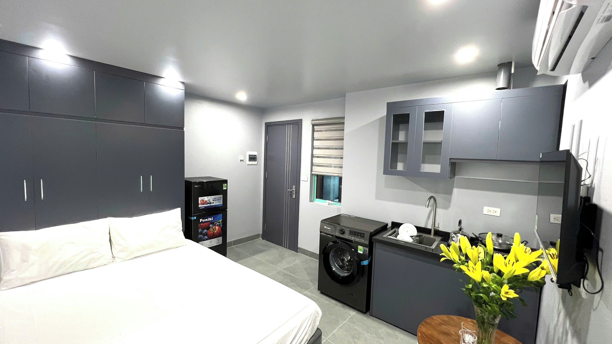 Habitación de hotel compacta con cama, lavadora, kitchenette pequeña y baño.