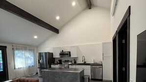 Eine moderne Küche mit weißen Schränken, einer zentralen Kochinsel und einem Essbereich mit braunem Sofa und Couchtisch.