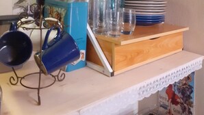 A kitchen counter with a wine bottle, glasses, a blue mug, and a shelf with salt and pepper shakers.