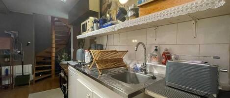 Une cuisine équipée d’un évier, d’étagères en bois et d’un escalier.