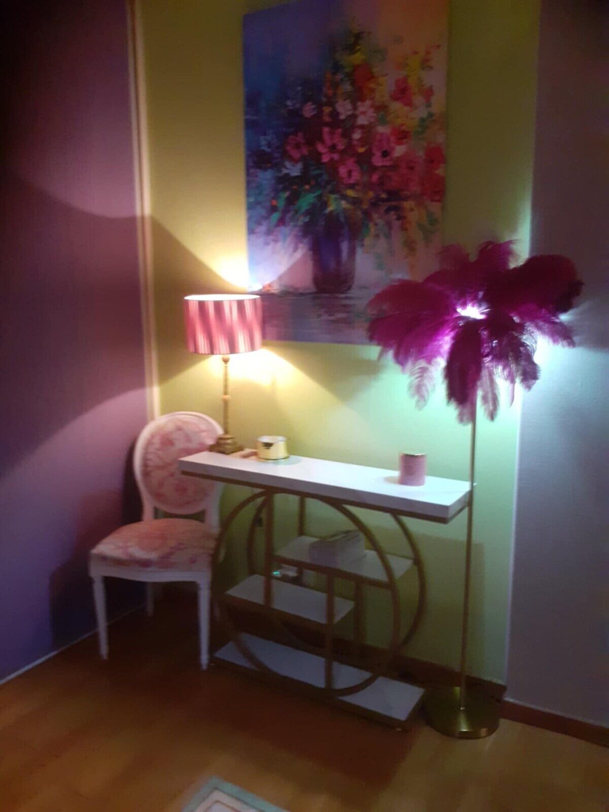 Una habitación con un escritorio blanco, una silla rosa, una lámpara de pie y un cuadro de flores en la pared.