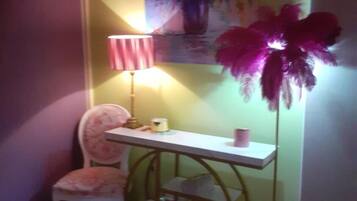 Una habitación con un escritorio blanco, una silla rosa, una lámpara de pie y un cuadro de flores en la pared.