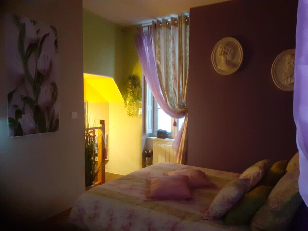 Quarto com cama, janela com cortinas, radiador e um quadro na parede.