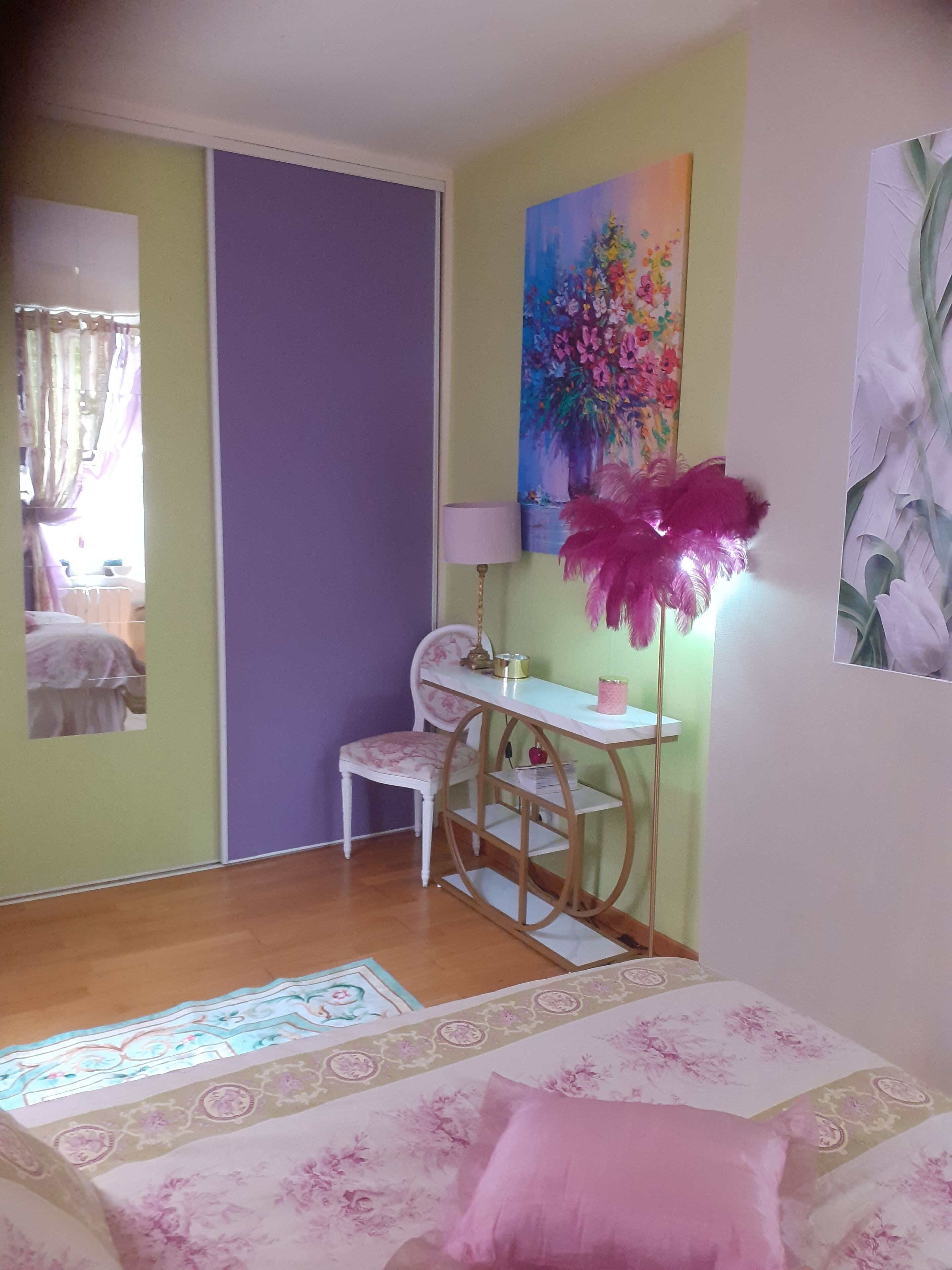 A bedroom with a bed, a desk, and a chair. There is a painting on the wall and a lamp on the desk.