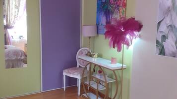A bedroom with a bed, a desk, and a chair. There is a painting on the wall and a lamp on the desk.
