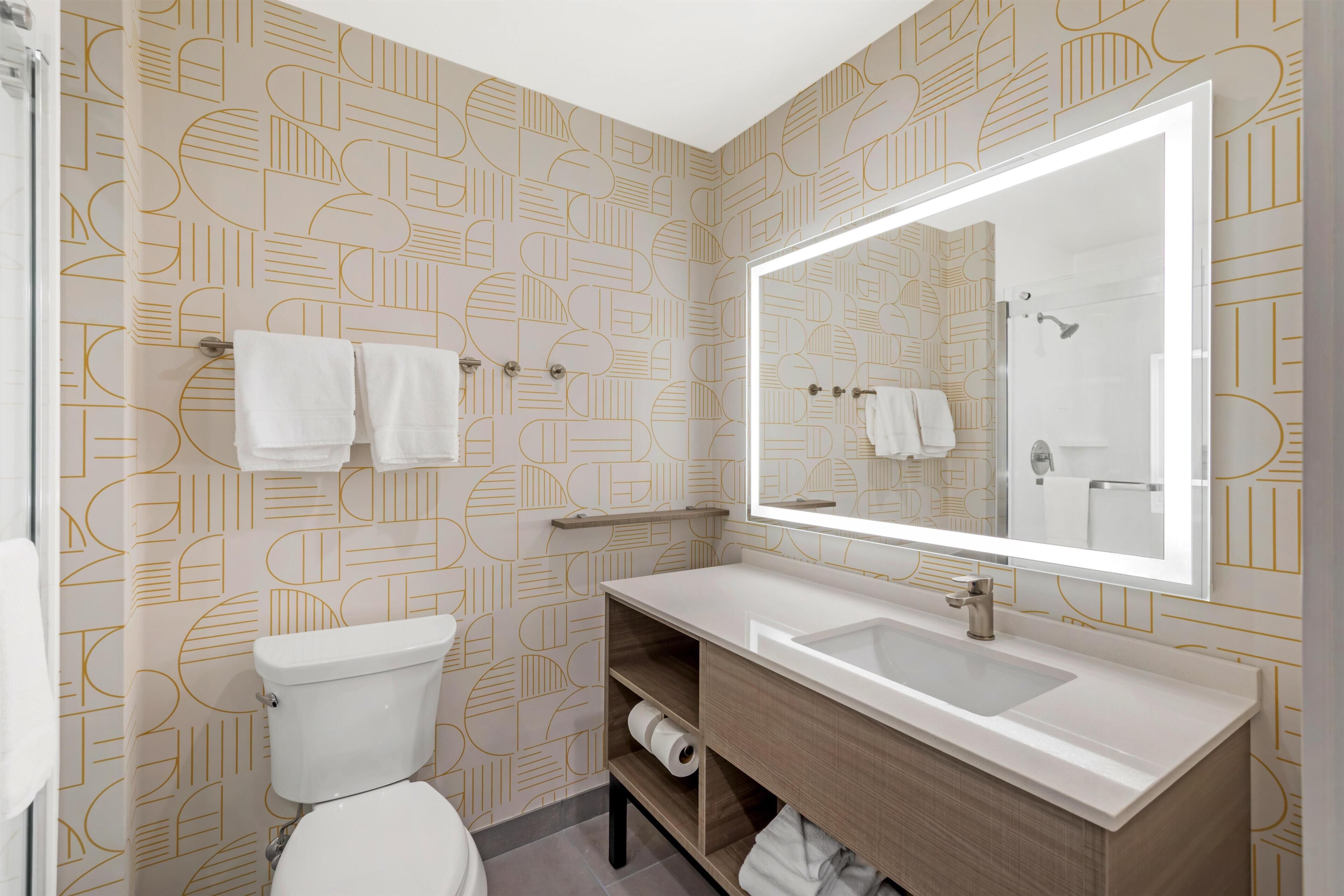 A bathroom with a toilet, a sink, a mirror, and patterned wallpaper.