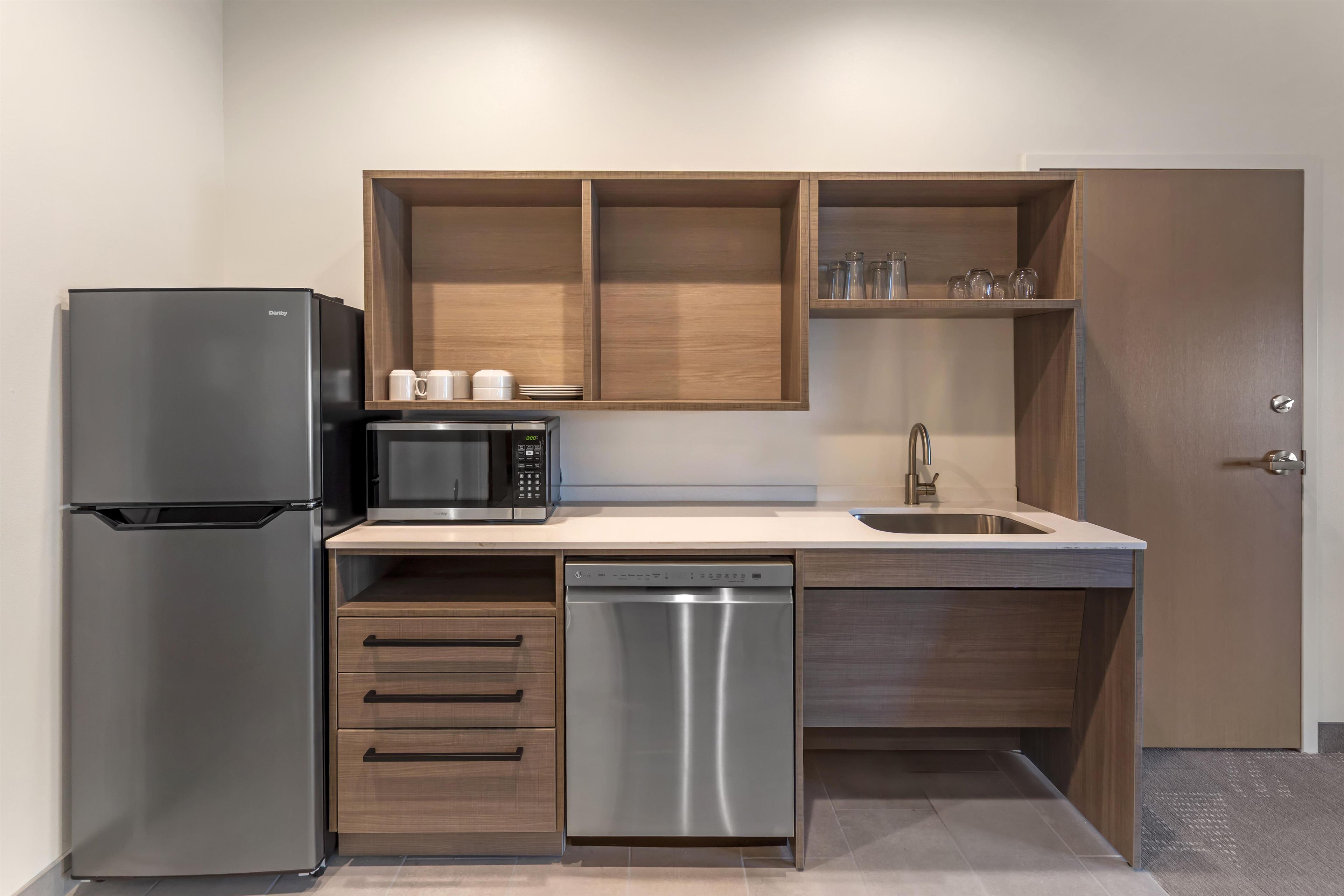 A compact kitchen with a refrigerator, microwave, dishwasher, and wooden cabinets.
