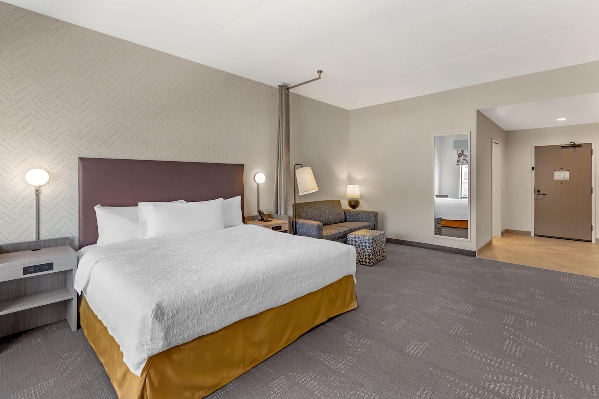 A hotel room with a large bed, bedside tables, a sofa, a mirror, and a door.