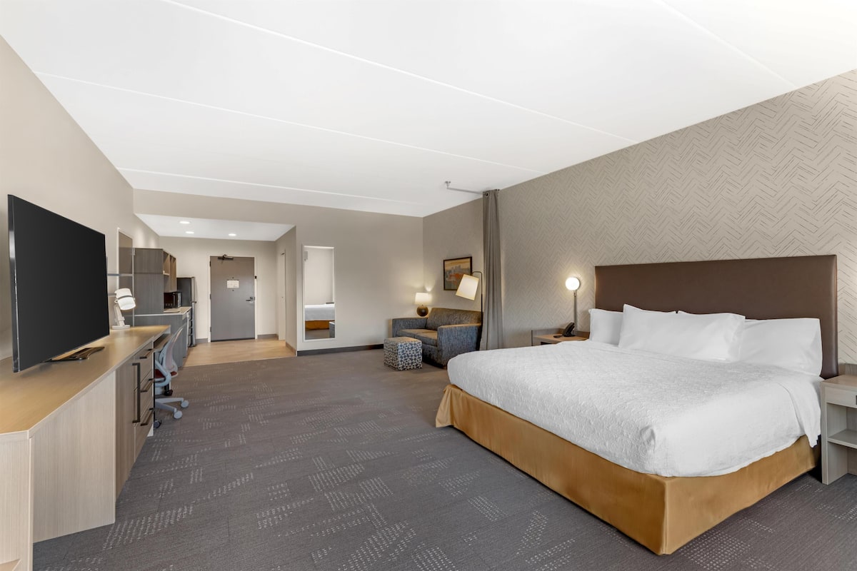 A hotel room with a large bed, a desk with a computer, a television, and a seating area with a chair and table.