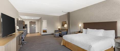 A hotel room with a large bed, a desk with a computer, a television, and a seating area with a chair and table.