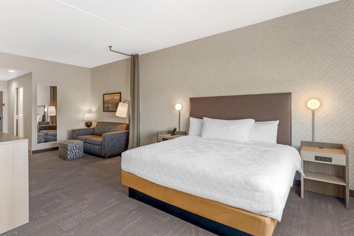 A hotel room with a large bed, a sofa, a desk, and a mirror.