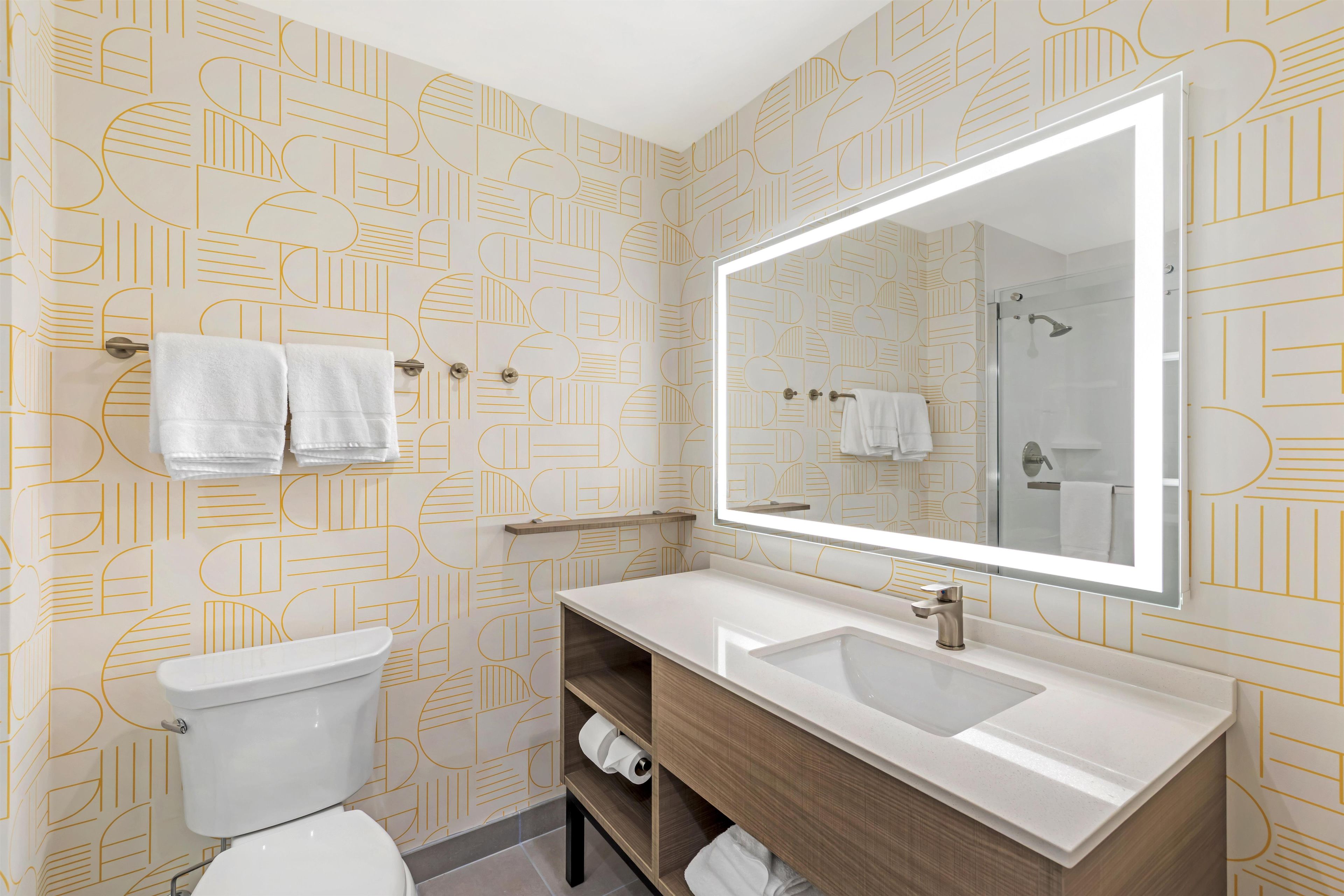 A bathroom with a toilet, sink, and mirror. There are towels hanging on a rack.