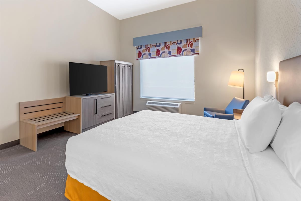 A hotel room with a bed, a TV, a desk, a lamp, and a window with curtains.
