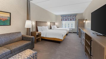 A hotel room with a sofa, two beds, a desk, a TV, and a painting on the wall.