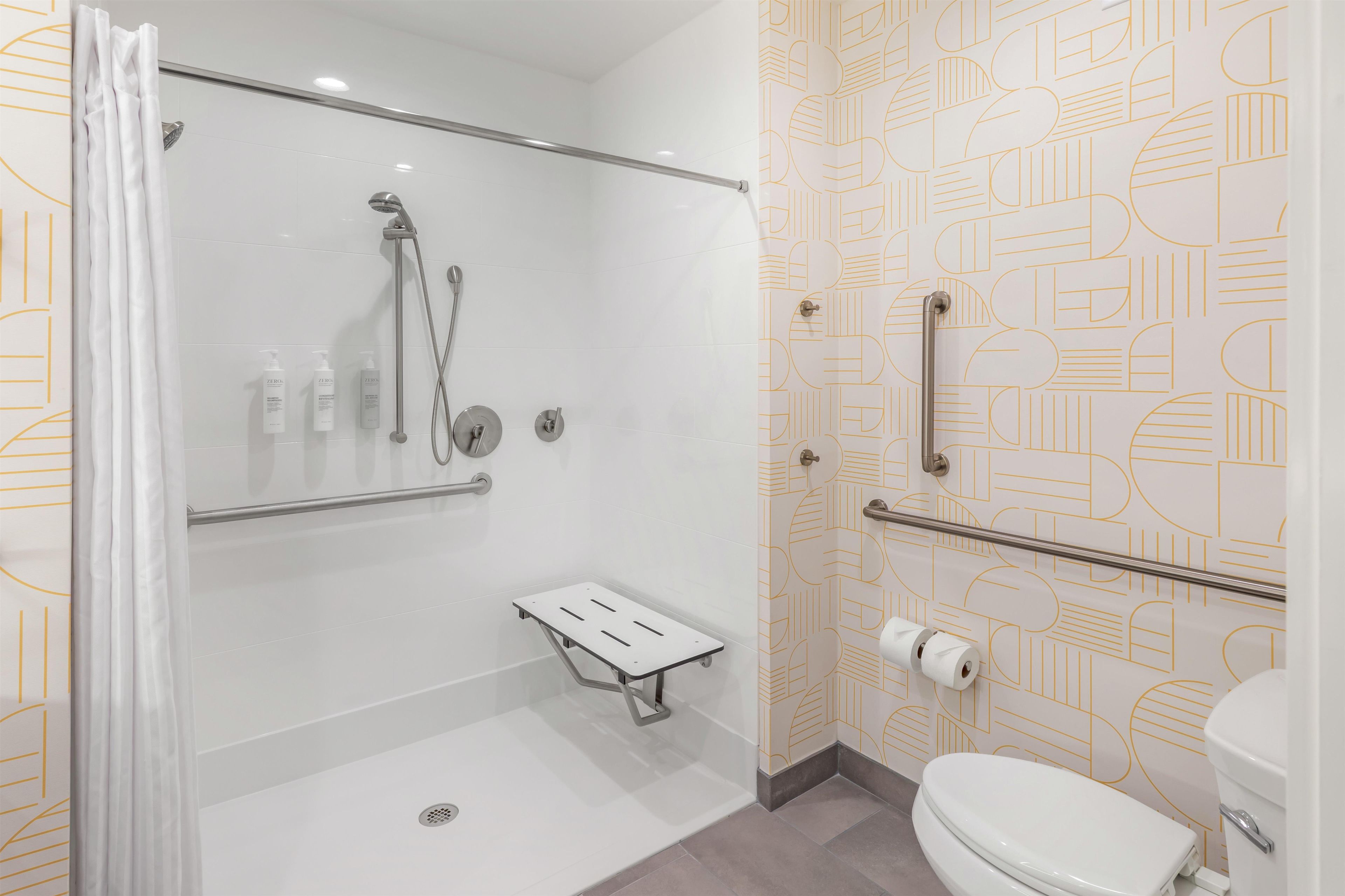 Un baño moderno con ducha, inodoro y barras de apoyo.