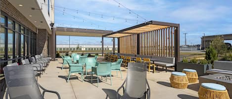 An outdoor seating area with various chairs and tables, a pergola structure, and a view of the sky.