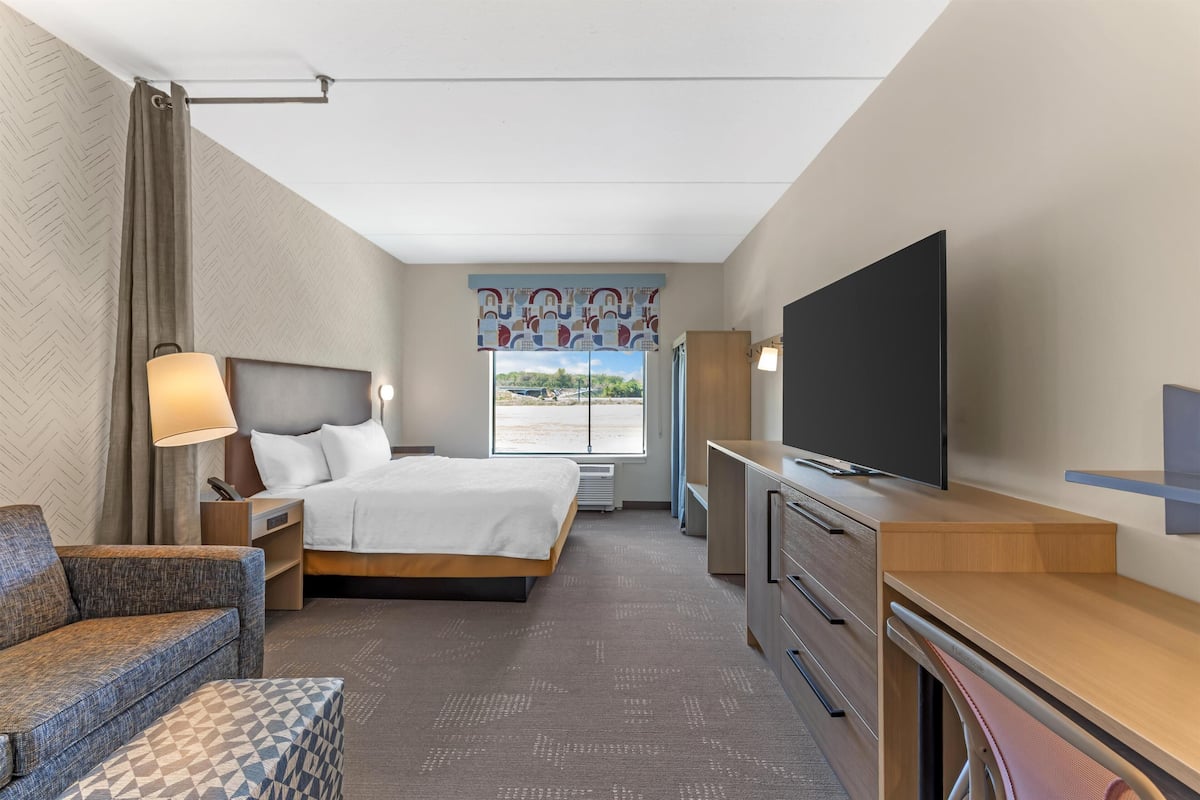 A hotel room with a bed, a TV, a desk, a chair, and a window with a view.