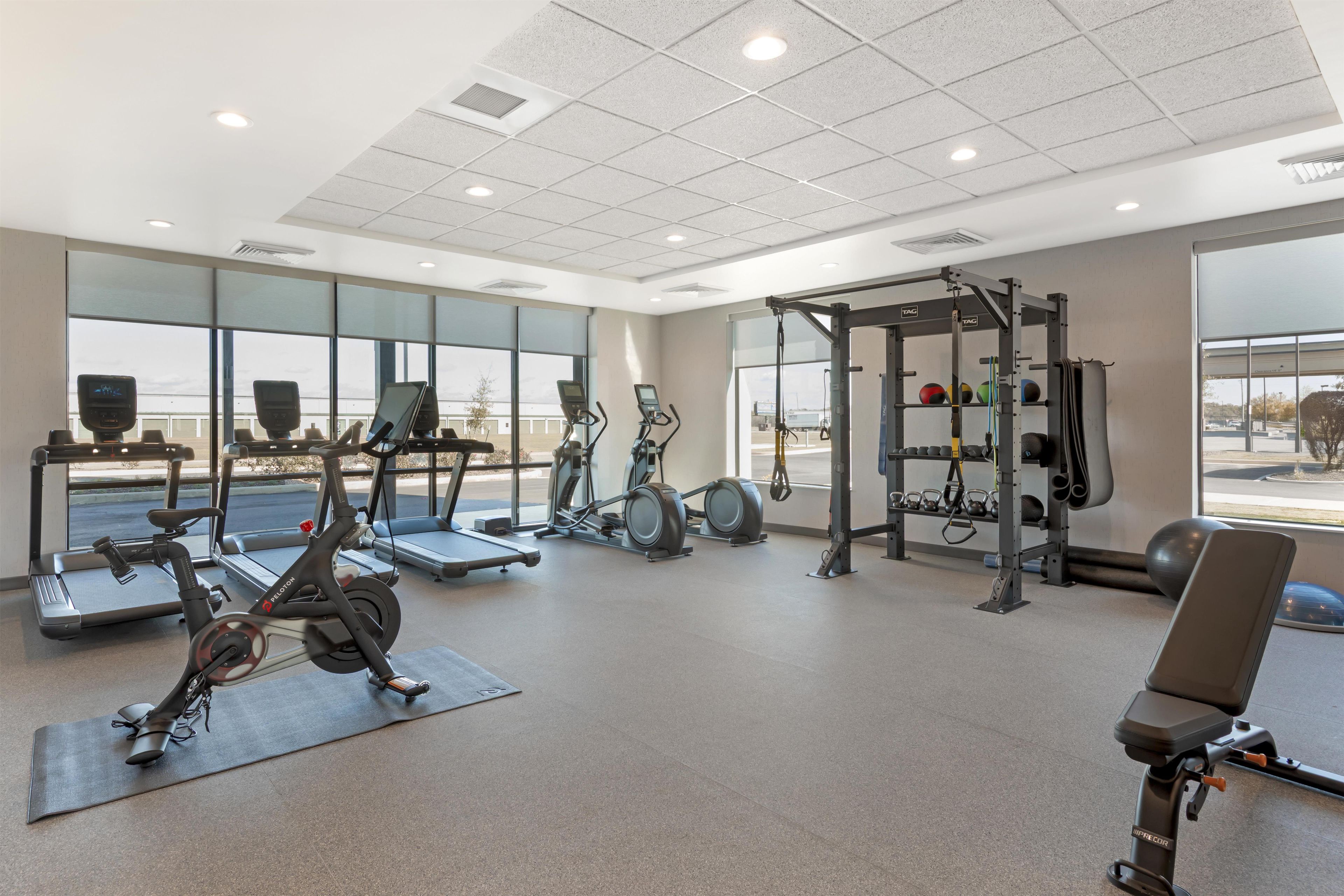 A gym with various exercise equipment, large windows, and a view of the outside.